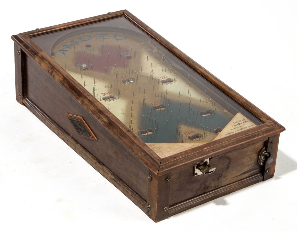 AMUZU TABLE-TOP ONE-CENT PINBALL MACHINE: AMUZU TABLE-TOP ONE-CENT PINBALL MACHINE, with label for the Caldwell Manufacturing Co., Lenoir, North Carolina. Circa 1930. 9 1/2" H, 31 1/4" L, 17" W. Provenance: From the estate collection of Floyd