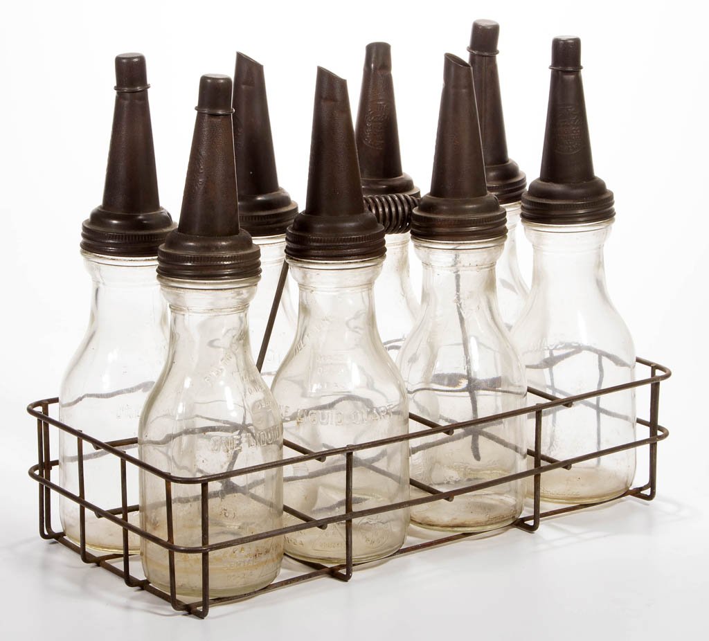 GLASS MOTOR OIL BOTTLES AND CARRIER: GLASS MOTOR OIL BOTTLES AND CARRIER, set of eight quart bottles with screw-on metal spouts, four with caps, in a wire-style carrier with low handle. First half 20th century. 14 1/2" HOA, 9" x 18" carr