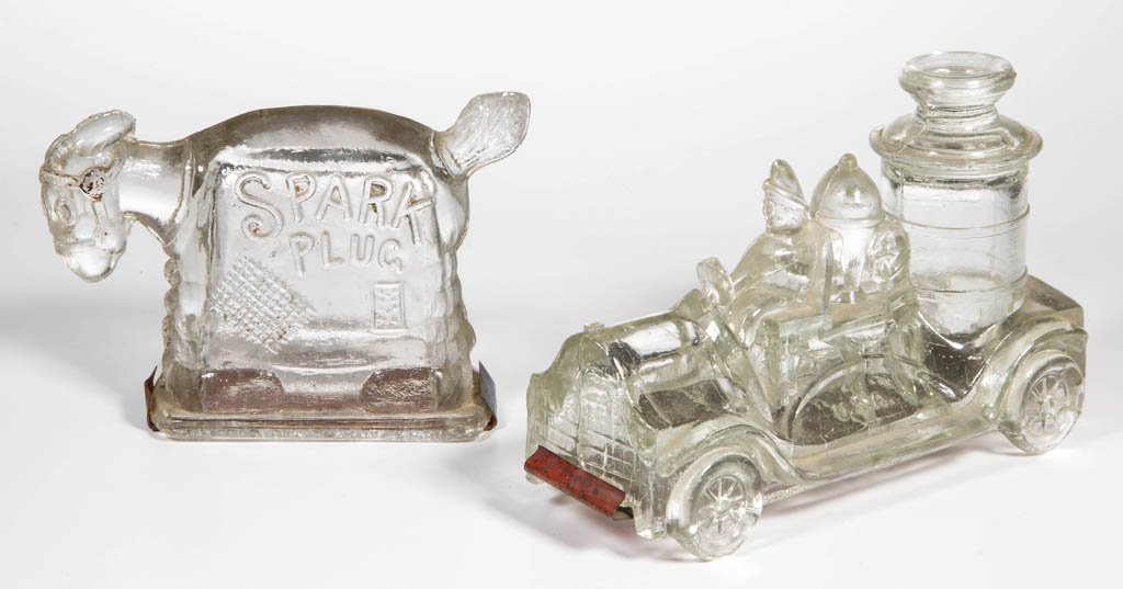 ASSORTED FIGURAL GLASS CANDY CONTAINERS, LOT OF TWO: ASSORTED FIGURAL GLASS CANDY CONTAINERS, LOT OF TWO, comprising a Spark Plug and a fire engine, each with embossed lettering and tin closure. Circa 1925. 3" and 3 1/4" H. Provenance: From a West Virgi