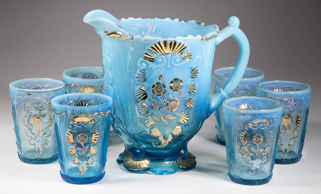 CARNELIAN (OMN) / EVERGLADES SEVEN-PIECE WATER SET: CARNELIAN (OMN) / EVERGLADES SEVEN-PIECE WATER SET, blue opalescent with gilt decoration, comprising a water pitcher and six tumblers. Northwood Glass Co. Circa 1903. 4" to 7 3/4" HOA. Literature: Hea
