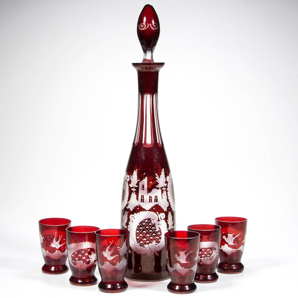 BOHEMIAN RUBY-STAINED AND ENGRAVED SEVEN-PIECE LIQUOR: BOHEMIAN RUBY-STAINED AND ENGRAVED SEVEN-PIECE LIQUOR SET, comprising a tapered decanter with original stopper and six glasses, with matching decorations including stag, birds, and castles. Late 19th/