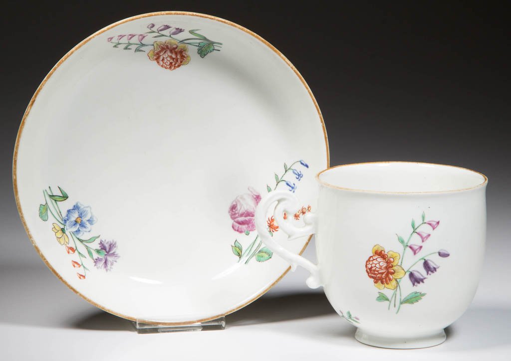 FRENCH CHANTILLY SOFT-PASTE PORCELAIN CUP AND SAUCER: FRENCH CHANTILLY SOFT-PASTE PORCELAIN CUP AND SAUCER, the footed cup with slightly-everted lip, with scrolling and curling handle, the footed saucer of plain form, both finely painted in polychrome en