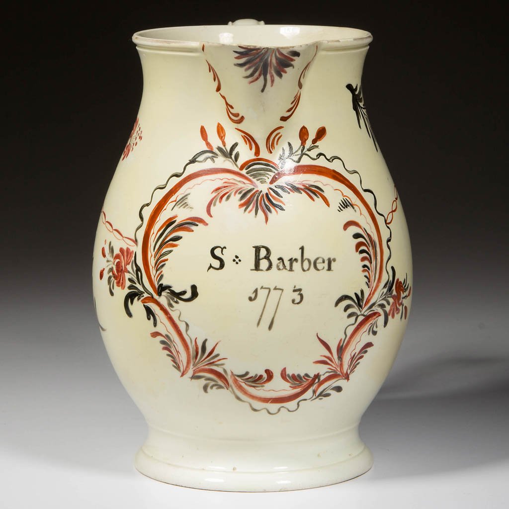 ENGLISH STAFFORDSHIRE POTTERY CREAMWARE CIDER PITCHER: ENGLISH STAFFORDSHIRE POTTERY CREAMWARE CIDER PITCHER, of pear-molded form on foot, with grooved, C-form handle, painted in iron-red and black with "S. Barber/1773" within elaborate foliate and scroll