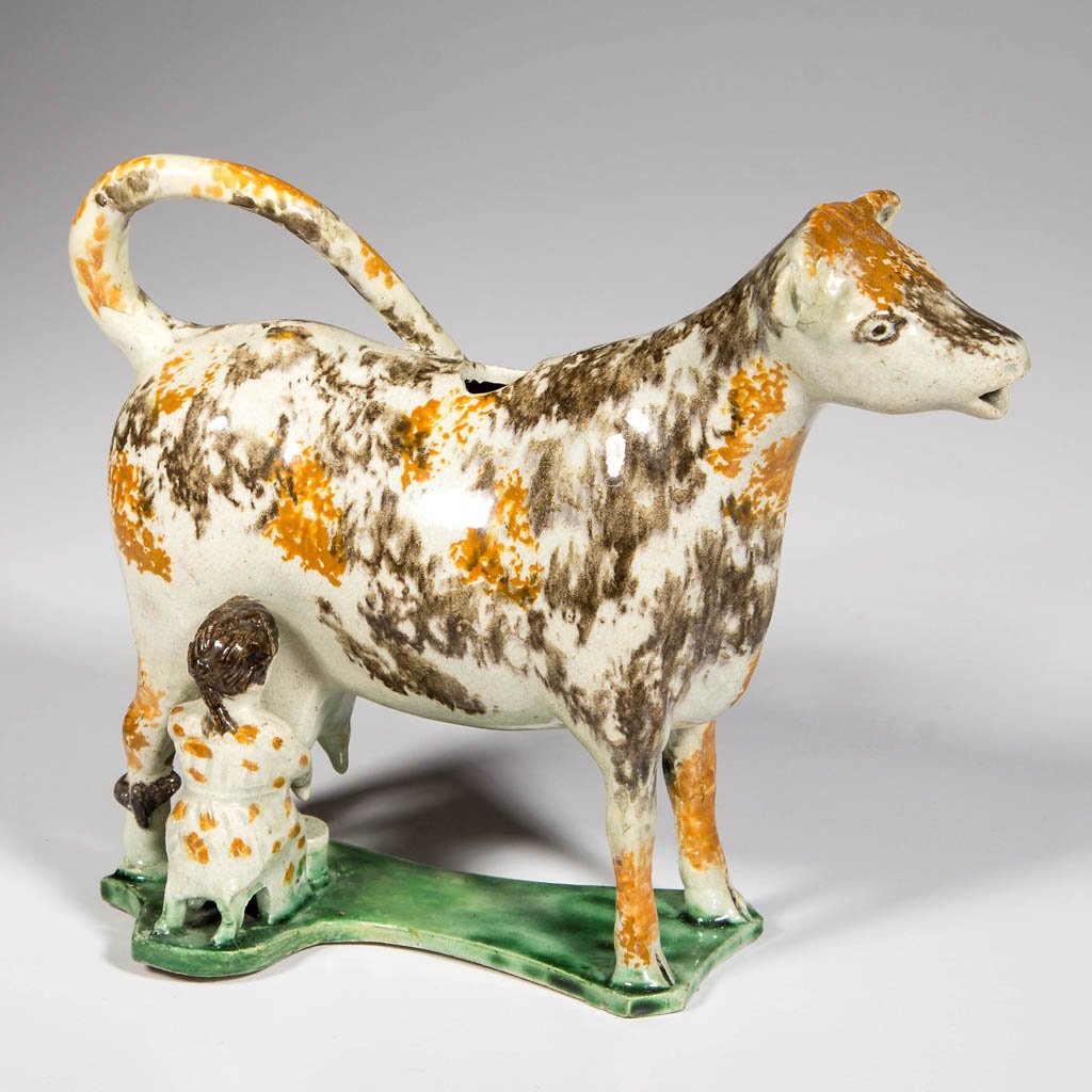 ENGLISH YORKSHIRE OR STAFFORDSHIRE POTTERY PEARLWARE: ENGLISH YORKSHIRE OR STAFFORDSHIRE POTTERY PEARLWARE COW CREAMER, modeled as a standing cow on an integrated flat base, with tail curled forward over back, being milked by a young maid on a stool, wit