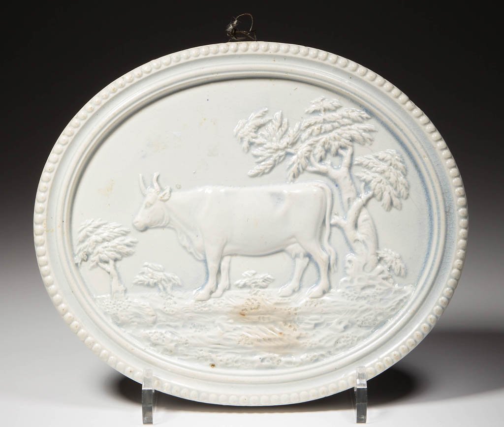 ENGLISH STAFFORDSHIRE POTTERY PEARLWARE COW PLAQUE: ENGLISH STAFFORDSHIRE POTTERY PEARLWARE COW PLAQUE, of ovular form, molded with a ring of beads to the edge, the inset center molded and sprigged with cow standing on a field near trees, unpainted. Un