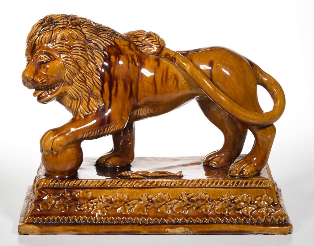 ENGLISH STAFFORDSHIRE POTTERY BUFF EARTHENWARE FIGURE: ENGLISH STAFFORDSHIRE POTTERY BUFF EARTHENWARE FIGURE OF A LION, standing, with one paw raised on an orb, its large tail curled on its back with tongue lolling from its open mouth, atop on a rectangul