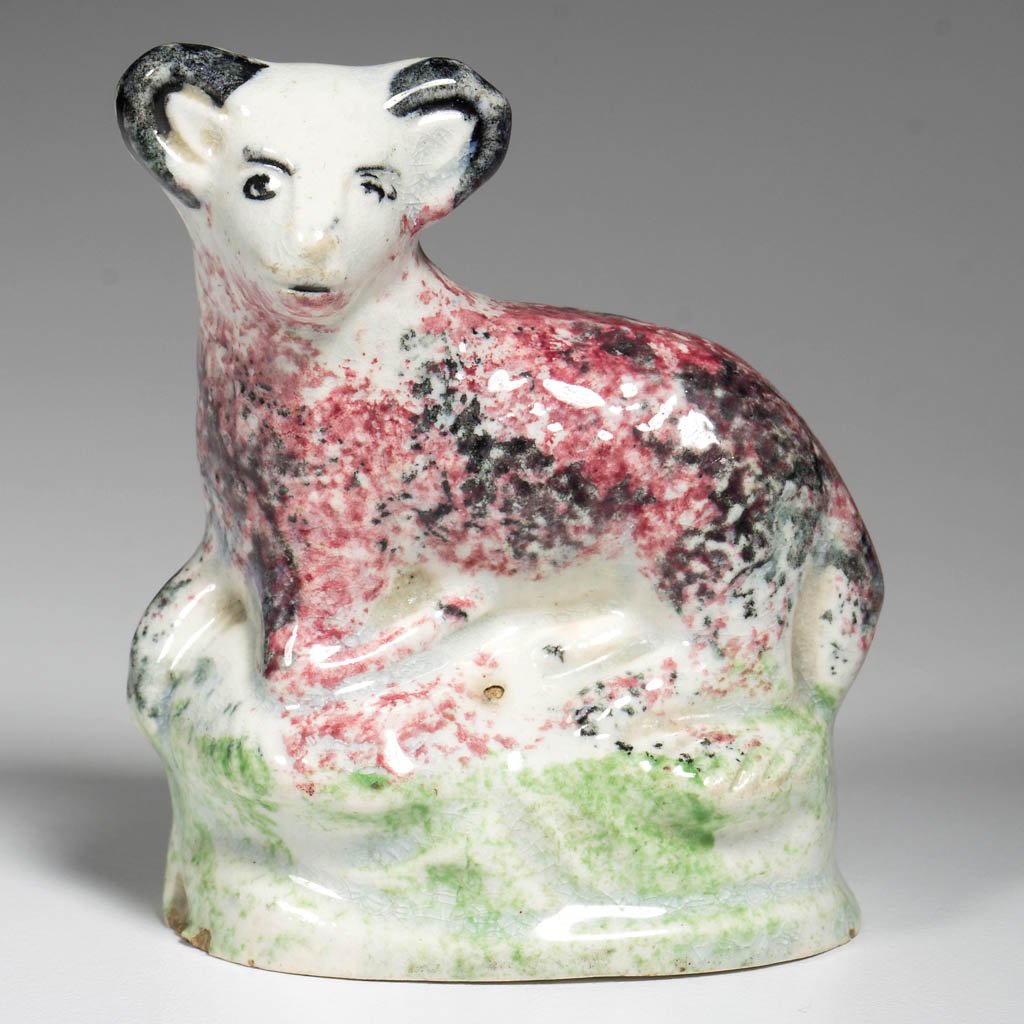 ENGLISH YORKSHIRE OR SCOTTISH POTTERY PEARLWARE FIGURE: ENGLISH YORKSHIRE OR SCOTTISH POTTERY PEARLWARE FIGURE OF A RECUMBENT LAMB, on an oval molded base, sponge-painted in typical Prattware hues with red and black splotches, with green splotchy base. Cir