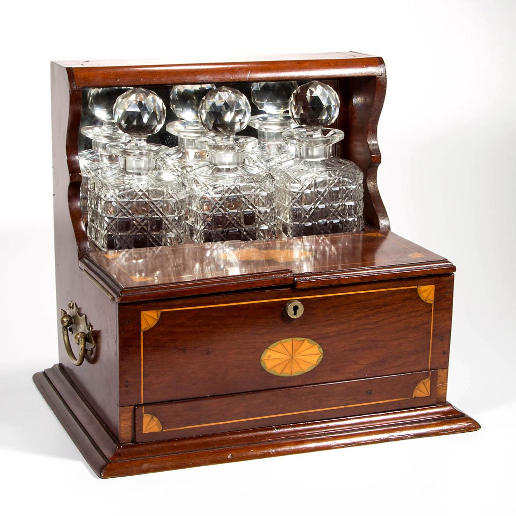 INLAID MAHOGANY TANTALUS: INLAID MAHOGANY TANTALUS, fitted with three glass bottles, inlay featuring central paterae and corner fans. Old surface with warm color. 20th century. 14" HOA, 13 1/4" WOA.Provenance: From an Augusta