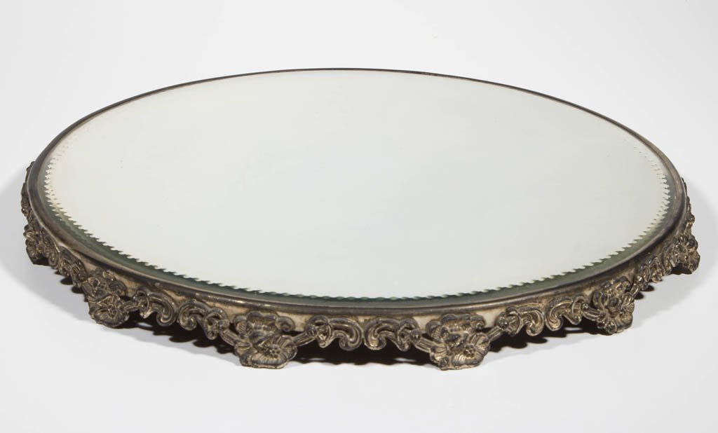 VICTORIAN SILVER-PLATE MIRROR PLATEAU: VICTORIAN SILVER-PLATE MIRROR PLATEAU, the silver-plated base with molded scroll and floral blossom design. Unmarked. 20th century. 1 1/2" H, 16 1/2" DOA. Provenance: From the Ed & Kay Winnick collect