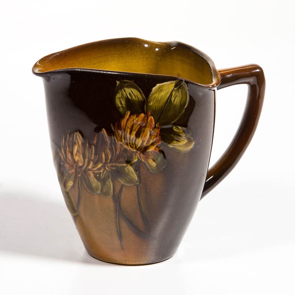ROOKWOOD ART POTTERY CREAMER: ROOKWOOD ART POTTERY CREAMER, standard glaze, with clover blossom and leaf decoration. Impressed Rookwood logo and other marks to underside, including possible artist's mark. 1894. 4" H.Provenance: Pr