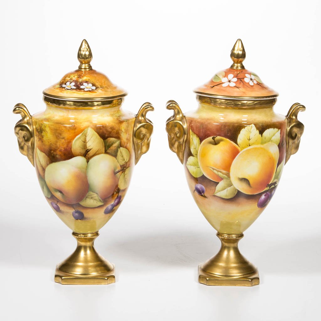 COALPORT, ENGLAND HAND-PAINTED PORCELAIN PAIR OF: COALPORT, ENGLAND HAND-PAINTED PORCELAIN PAIR OF COVERED URNS, each footed form with ram's head mask handles, decorated with fruit, artist signed "L. Dale" for Lynda Dale, and "J. Mottram" for Joseph 