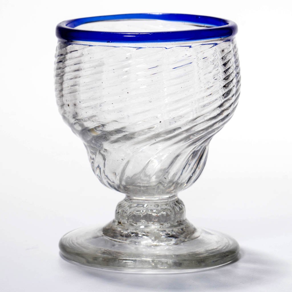 PATTERN-MOLDED RIB FOOTED OPEN SALT: PATTERN-MOLDED RIB FOOTED OPEN SALT, colorless with applied sapphire blue rim, double-ogee bowl with 18 ribs swirled to the right, raised on a short ribbed, compressed-knop stem and applied circular s