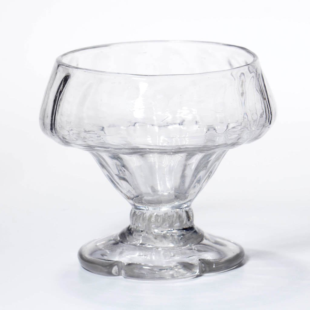PATTERN-MOLDED RIB FOOTED OPEN SALT: PATTERN-MOLDED RIB FOOTED OPEN SALT, colorless, double-ogee bowl patterned with 17 vertical ribs, raised on a short thick stem and an applied circular sloping foot with a scalloped edge, with a rough 
