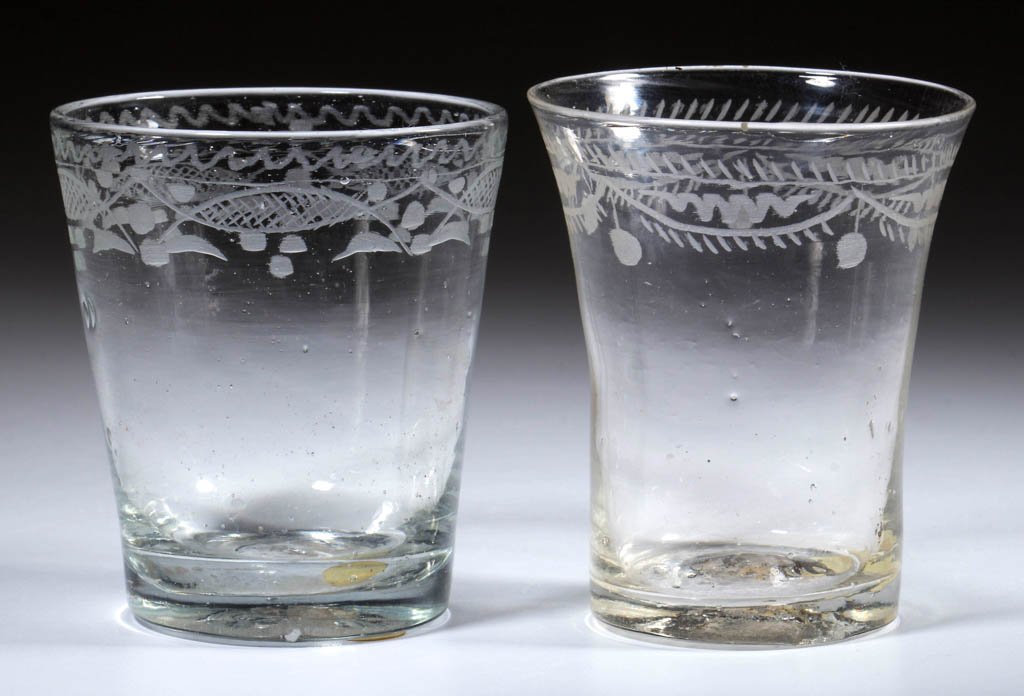 FREE-BLOWN AND ENGRAVED DIMINUTIVE TUMBLERS, LOT OF TWO: FREE-BLOWN AND ENGRAVED DIMINUTIVE TUMBLERS, LOT OF TWO, colorless, comprising a flared example with fringed swags and tassels below rim, and a tapered example featuring so-called Stiegel decoration b