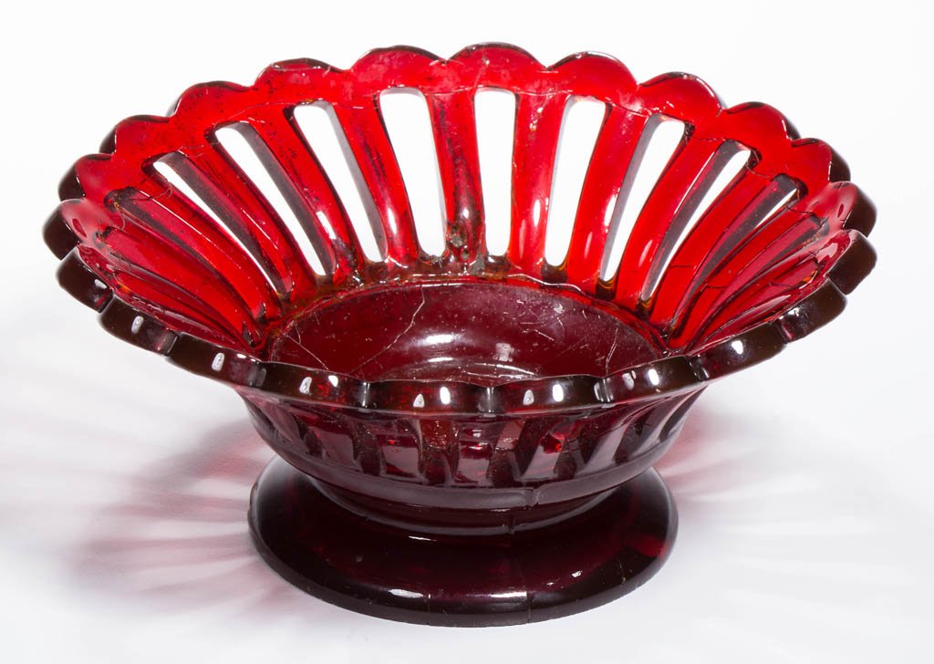 PRESSED OPEN-WORK DISH ON LOW FOOT: PRESSED OPEN-WORK DISH ON LOW FOOT, deep brilliant ruby with opalescent bloom to the base, flared 22-scallop rim and conforming staves surrounding the plain center, raised on a circular foot with poli