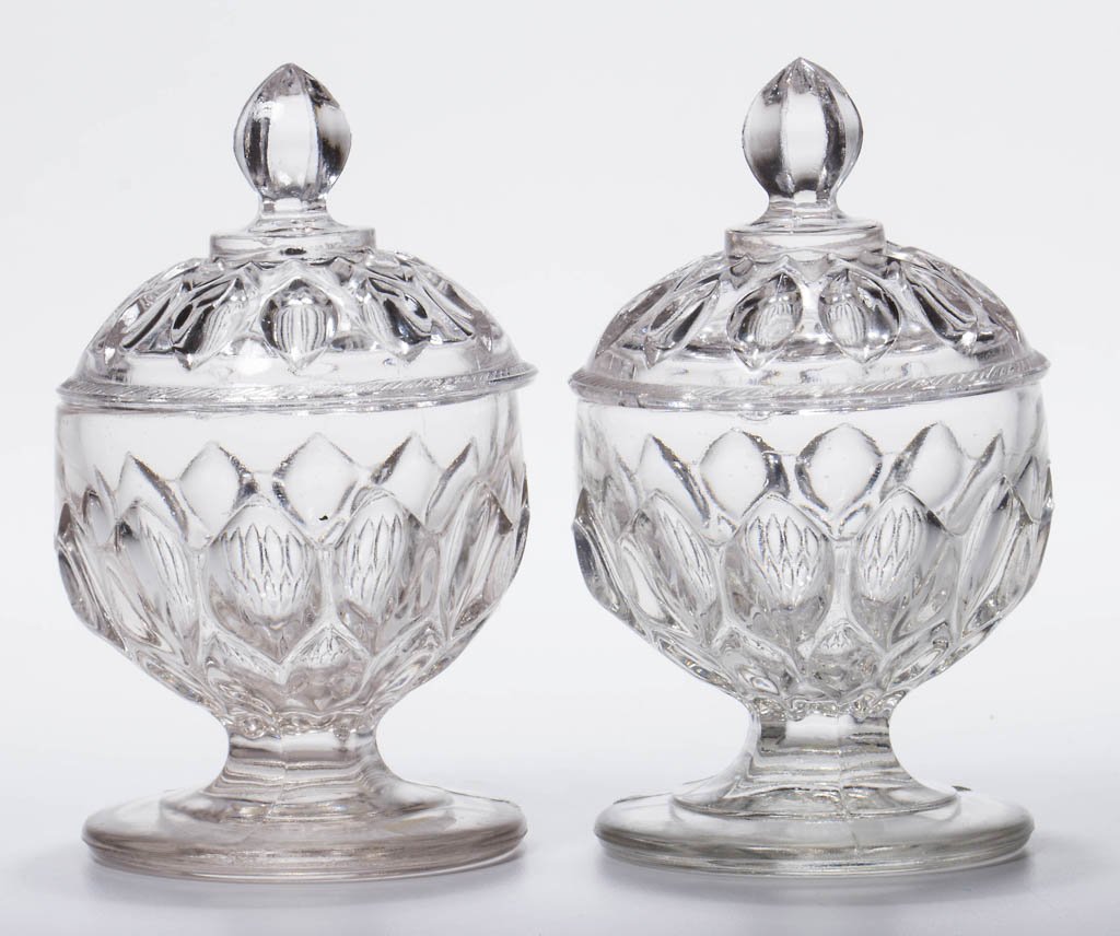 ALMOND THUMBPRINT PAIR OF PRESSED COVERED MASTER SALTS: ALMOND THUMBPRINT PAIR OF PRESSED COVERED MASTER SALTS, colorless lead glass, each pedestal-form with plain foot, covers with rope-edge rim and hexagonal finial. Third quarter 19th century. 4 1/4" HOA