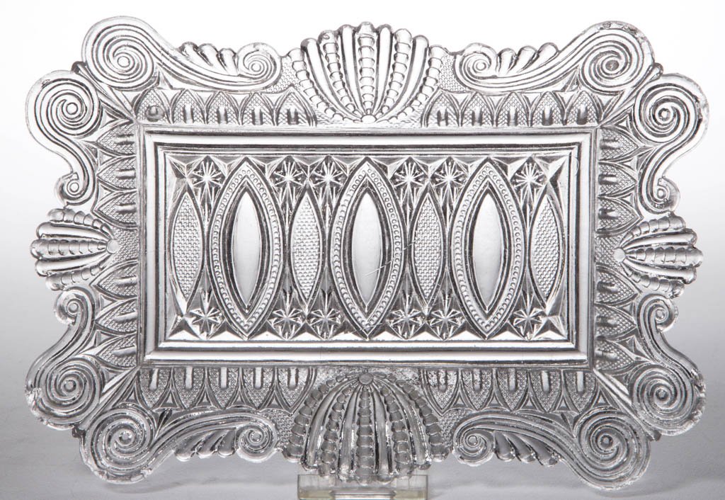 PRESSED LACY LANCET AND LEAF RECTANGULAR RAY: PRESSED LACY LANCET AND LEAF RECTANGULAR RAY, colorless, complex-shaped rim, shoulder featuring scrolls, shells, and gothic arches, center with ellipses and stars. Pittsburgh area. Circa 1830-1840. 1 