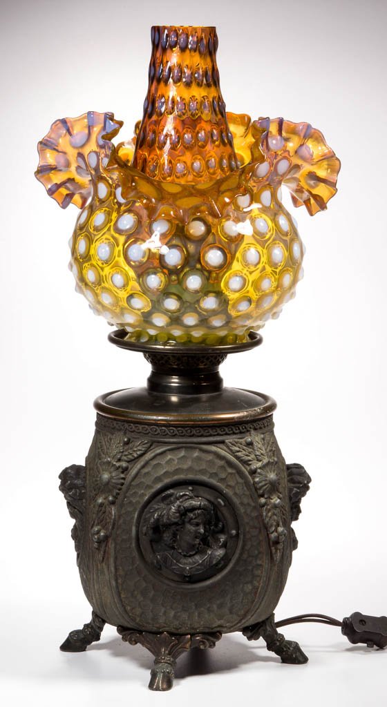 HIGH-RELIEF BUST METAL KEROSENE LAMP: HIGH-RELIEF BUST METAL KEROSENE LAMP, heavy cast metal, four-sided base, with hammered panels each centering a bust in relief, cornered with floral and leaf decoration, on four hoof feet. Fitted with 