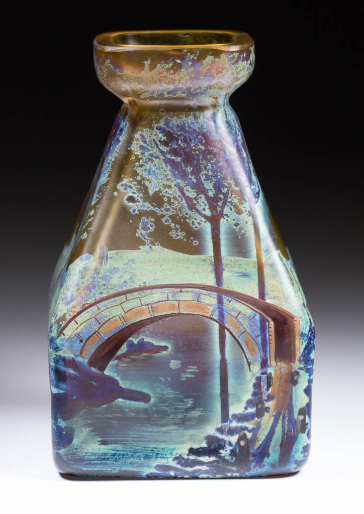 STAINED ART GLASS VASE: STAINED ART GLASS VASE, amber with polychrome-staining, having a square base and tapered neck, depicting a bridge over a stream and surrounding forest. Late 19th/first quarter 20th century. 4 1/2" H, 