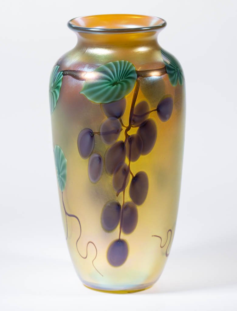ORIENT AND FLUME GRAPES STUDIO ART GLASS VASE: ORIENT AND FLUME GRAPES STUDIO ART GLASS VASE, gold iridescent, urn-form with two grape bunches bordered by brown vines and green leaves, signed, "Orient & Flume/1985/A27." 1985. 10" H.Provenance: Fro