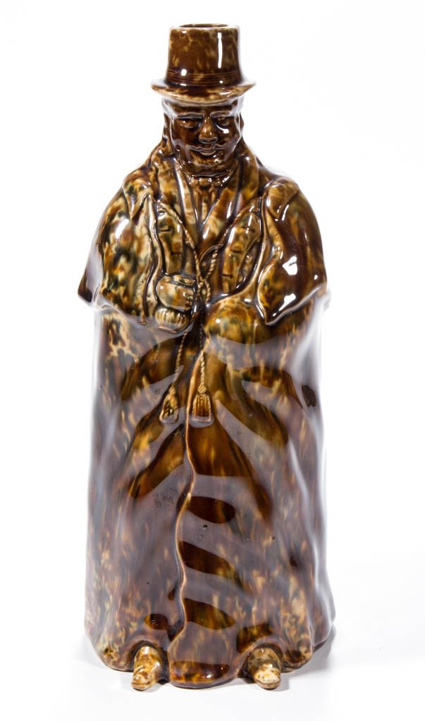 BENNINGTON FLINT-ENAMEL POTTERY COACHMAN BOTTLE: BENNINGTON FLINT-ENAMEL POTTERY COACHMAN BOTTLE, mottled brown with blue-green and some orange, well detailed gentleman with moustache, holding a bottle, cape with tassels. Unmarked. Lyman, Fenton & C