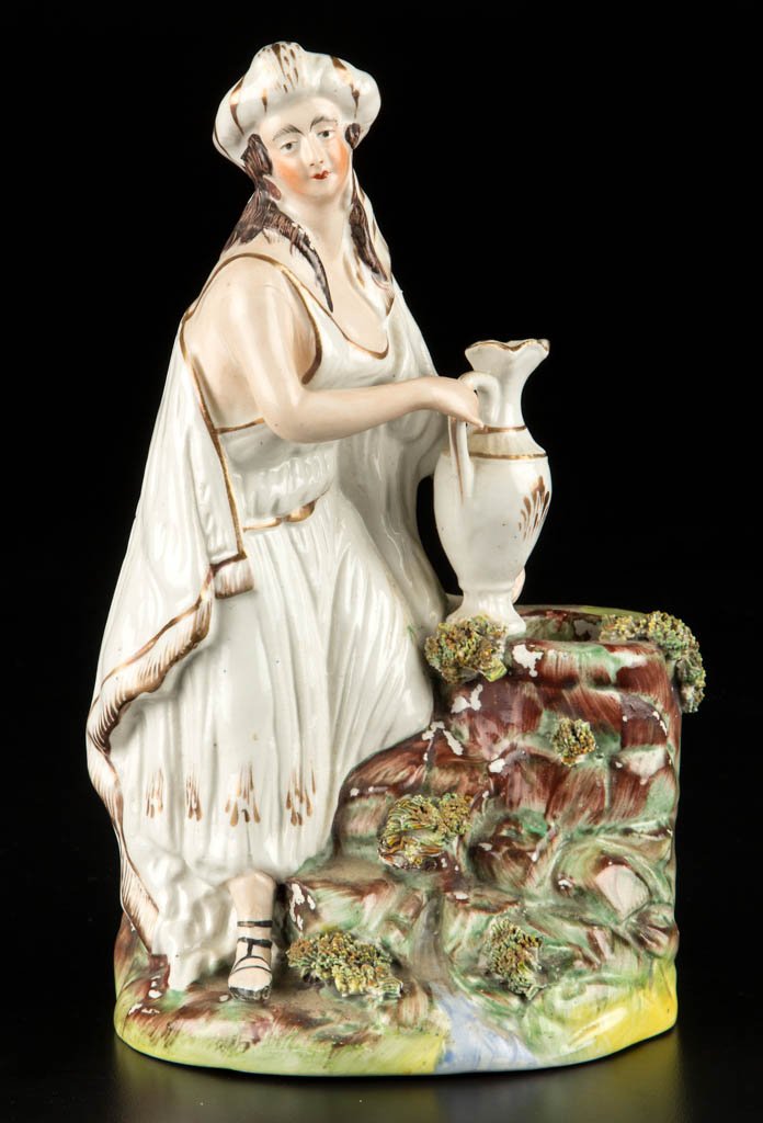 ENGLISH STAFFORDSHIRE POTTERY FIGURE OF REBECCA AT THE: ENGLISH STAFFORDSHIRE POTTERY FIGURE OF REBECCA AT THE WELL, standing, holding a ewer over the well, atop a stepped oval mound base with applied splotches of dried clay "grass," her figure and the ewe