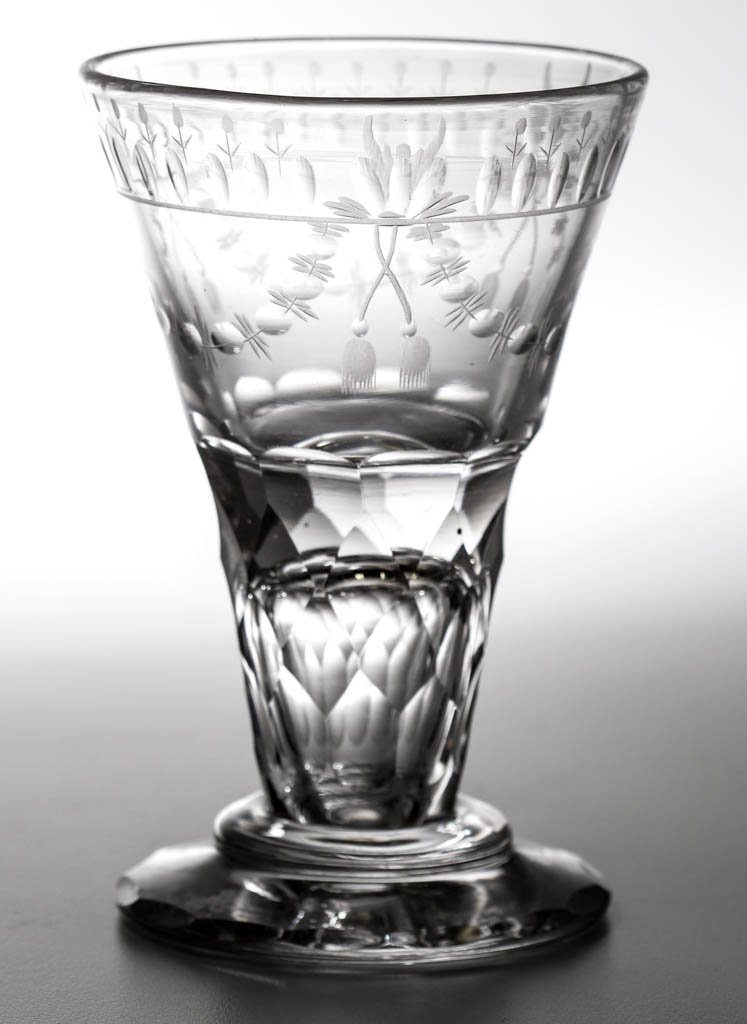 CONTINENTAL FREE-BLOWN, CUT, AND ENGRAVED TOASTMASTER'S: CONTINENTAL FREE-BLOWN, CUT, AND ENGRAVED TOASTMASTER'S / FIRING GLASS, colorless non-lead glass, trumpet form, swag and tassel decoration on bowl, raised on a facet-cut hollow stem, circular foot wit