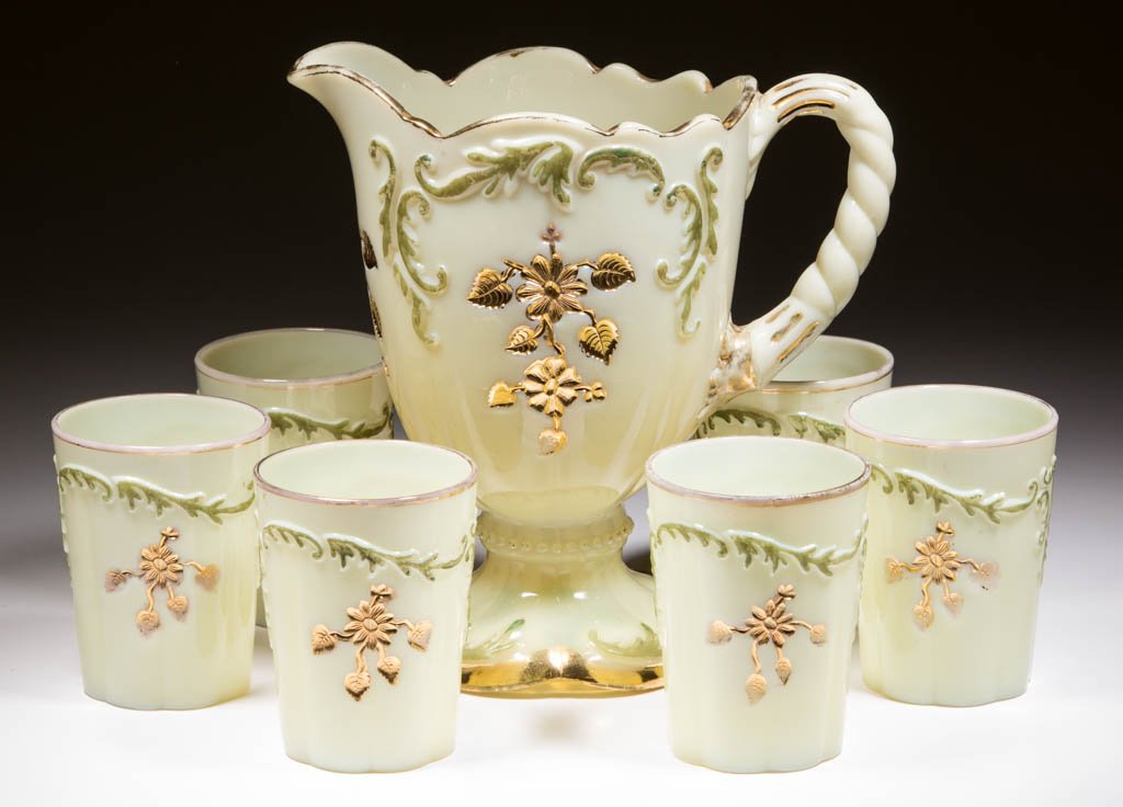 INTAGLIO SEVEN-PIECE WATER SET: INTAGLIO SEVEN-PIECE WATER SET, custard with green stain and gilt decoration, comprising a water pitcher and six tumblers. Northwood Glass Co. Circa 1898-1902. 3 7/8" to 8 1/2" H. Literature: Parallel