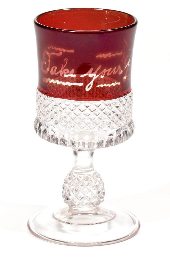 SUPERIOR - RUBY-STAINED TOOTHPICK HOLDER: SUPERIOR - RUBY-STAINED TOOTHPICK HOLDER, colorless, wine-form on circular foot, with resist-like decoration and lettering "Take your pick." U. S. Glass Co. Circa 1896. 3 7/8" H.Literature: Parallels