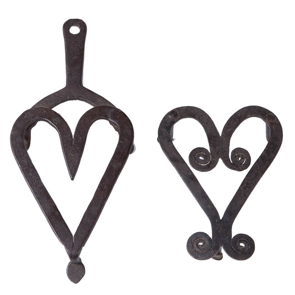 SOUTHERN WROUGHT-IRON PRESSING-IRON TRIVETS, LOT OF TWO: SOUTHERN WROUGHT-IRON PRESSING-IRON TRIVETS, LOT OF TWO, each with heart motif raised on three legs terminating in penny feet, one with handle. Original surfaces. Probably eastern Tennessee or southwe