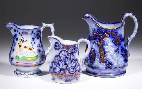 ENGLISH FLOW BLUE LUSTRE CERAMIC PITCHERS, LOT OF THREE: ENGLISH FLOW BLUE LUSTRE CERAMIC PITCHERS, LOT OF THREE, having molded foliate designs and deer on one with blue coloring and copper lustre, molded handles. Copper lustre decorator's marks on the