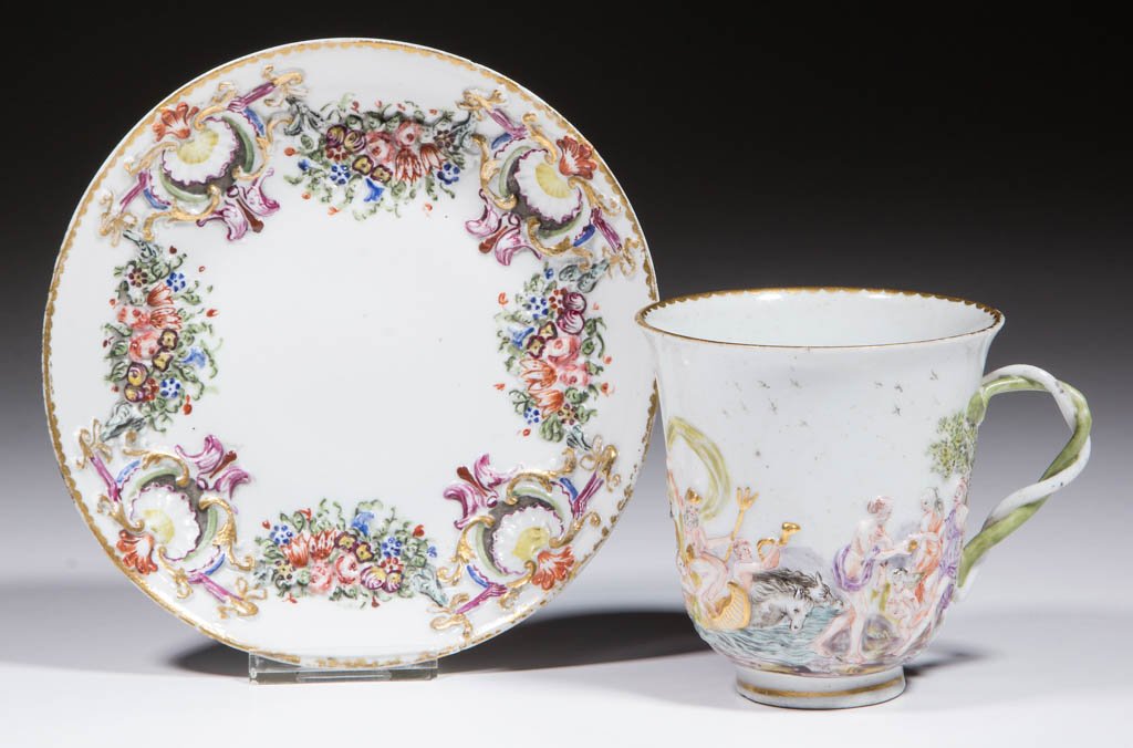 ITALIAN DOCCIA CAPODIMONTE CERAMIC CUP AND SAUCER: ITALIAN DOCCIA CAPODIMONTE CERAMIC CUP AND SAUCER, having classical molded designs on mug and swags of floral and shell designs on saucer with polychrome enamels and gilding. Unmarked. Likely Doccia,