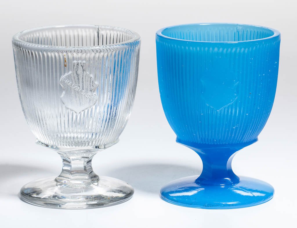 FINE RIB / REEDED (OMN) EGG CUPS / POMADE BASES, LOT OF: FINE RIB / REEDED (OMN) EGG CUPS / POMADE BASES, LOT OF TWO, comprising a translucent starch blue example with plain shield and a colorless lead glass example with "PHALON & SON" on shield. Boston & S