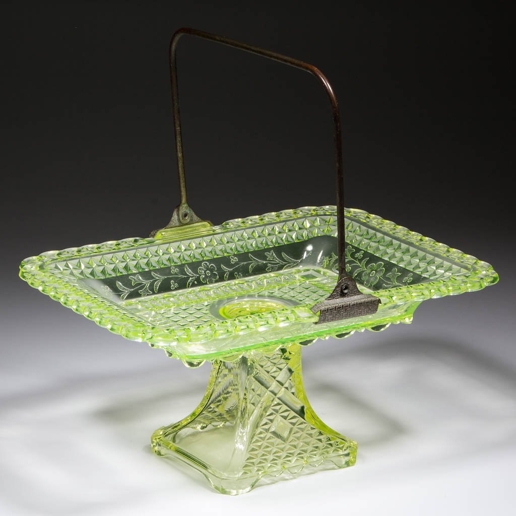 ADAMS NO. 140 / WILDFLOWER CAKE BASKET: ADAMS NO. 140 / WILDFLOWER CAKE BASKET, Vaseline (black lighted), original metal handle. Adams & Co. Circa 1874. 5 1/8" H, 7 3/4" x 10 7/8". Undamaged. Provenance: Collection of William D. "Bill" Ross