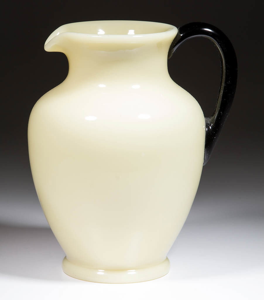 STEUBEN ART GLASS WATER PITCHER: STEUBEN ART GLASS WATER PITCHER, Ivory, shape 7218, with an applied Mirror Black handle, polished pontil mark, unsigned. Steuben Glass Works. Circa 1925. 9 1/4" H, 5" DOA rim, 4" D base. Undamaged. Li