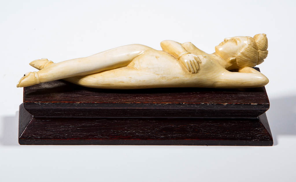 ASIAN CARVED EROTIC FIGURE: ASIAN CARVED EROTIC FIGURE, reclining female nude in amorous posture, attached to a shaped wooden base. Late 19th/early 20th century. 4 3/4" LOA. Figure in good condition with some age cracks and mino