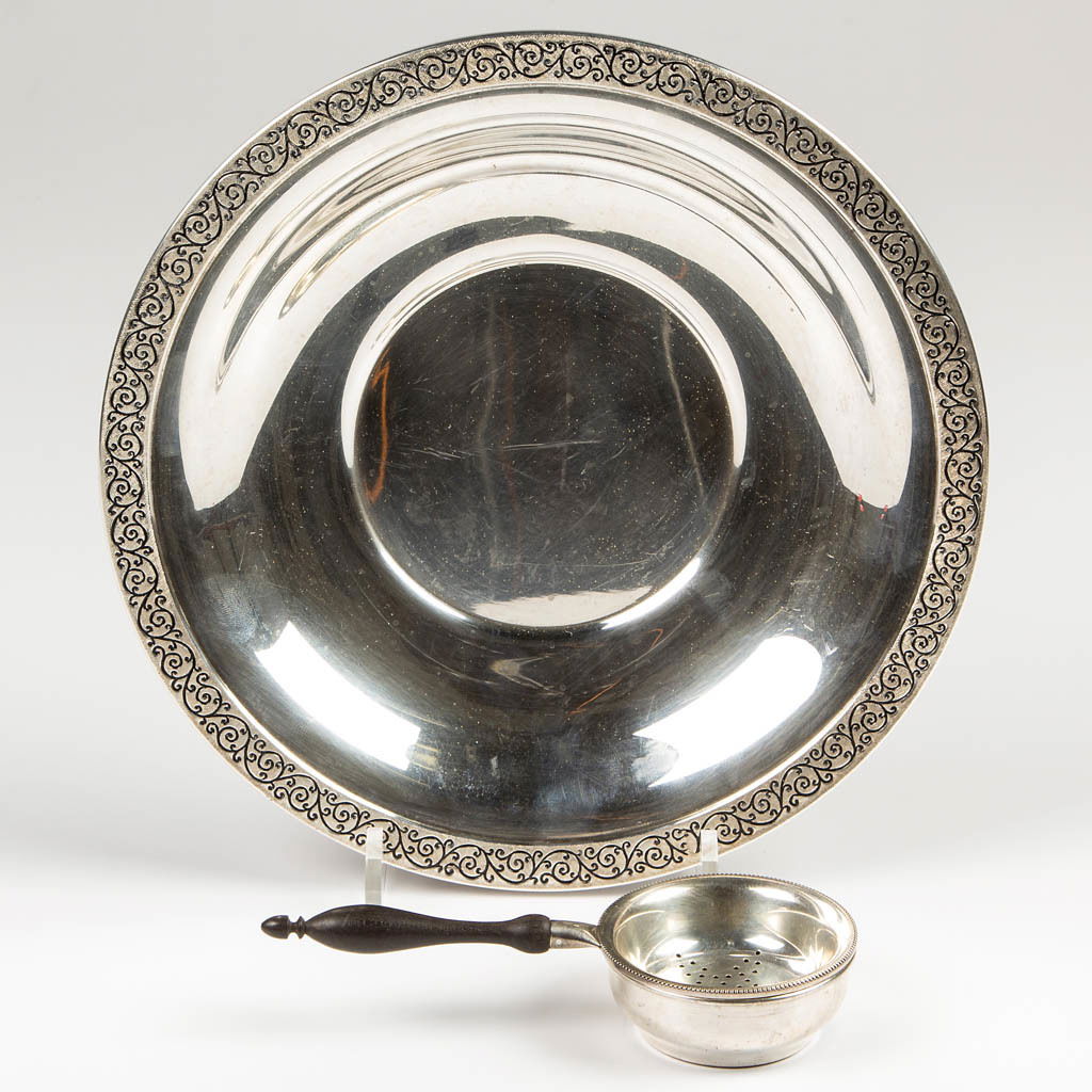 ASSORTED STERLING SILVER ARTICLES, LOT OF THREE: ASSORTED STERLING SILVER ARTICLES, LOT OF THREE, comprising a tea strainer with ebony wood handle and drip bowl, and a plate with decorated rim. Total weight: 8.0 ozt. 20th century. 2 5/8" and 9 1/2"