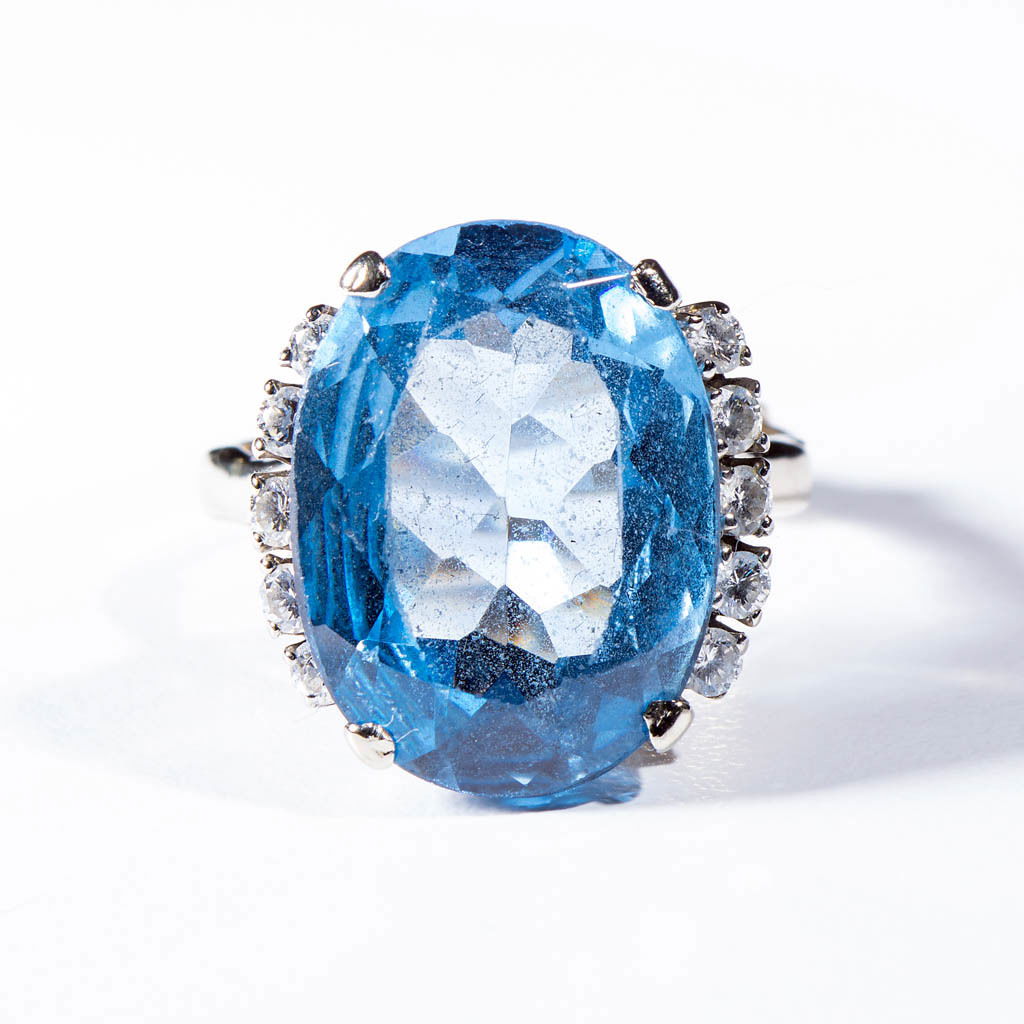 VINTAGE LADY'S 14K WHITE GOLD AND TOPAZ RING: VINTAGE LADY'S 14K WHITE GOLD AND TOPAZ RING, marked, basket-style setting with large, 13mm x 20mm oval blue sapphire flanked by five melee diamonds on wide sides. Total weight: 6.0 dwt. 20th century.
