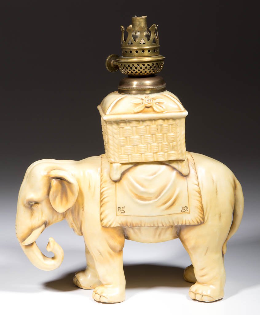 PORCELAIN STANDING ELEPHANT FIGURAL MINIATURE LAMP: PORCELAIN STANDING ELEPHANT FIGURAL MINIATURE LAMP, tan/brown tones ground with realistic features and shading, drop-in porcelain square-form basket (font), underside edge stamped "VU", underside of o