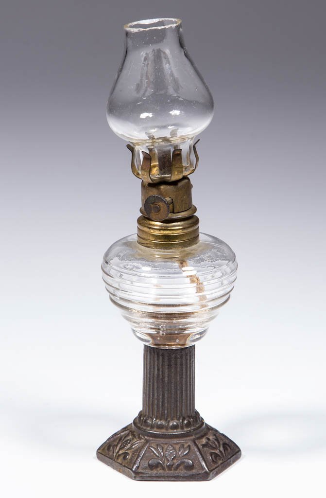 LITTLE CROWN MINIATURE STAND LAMP: LITTLE CROWN MINIATURE STAND LAMP, colorless pyriform font with ribs, cast-iron ribbed stem and hexagonal foot with fleur-de-lis embossing, colorless chimney-shade, period collar. Fitted with a period