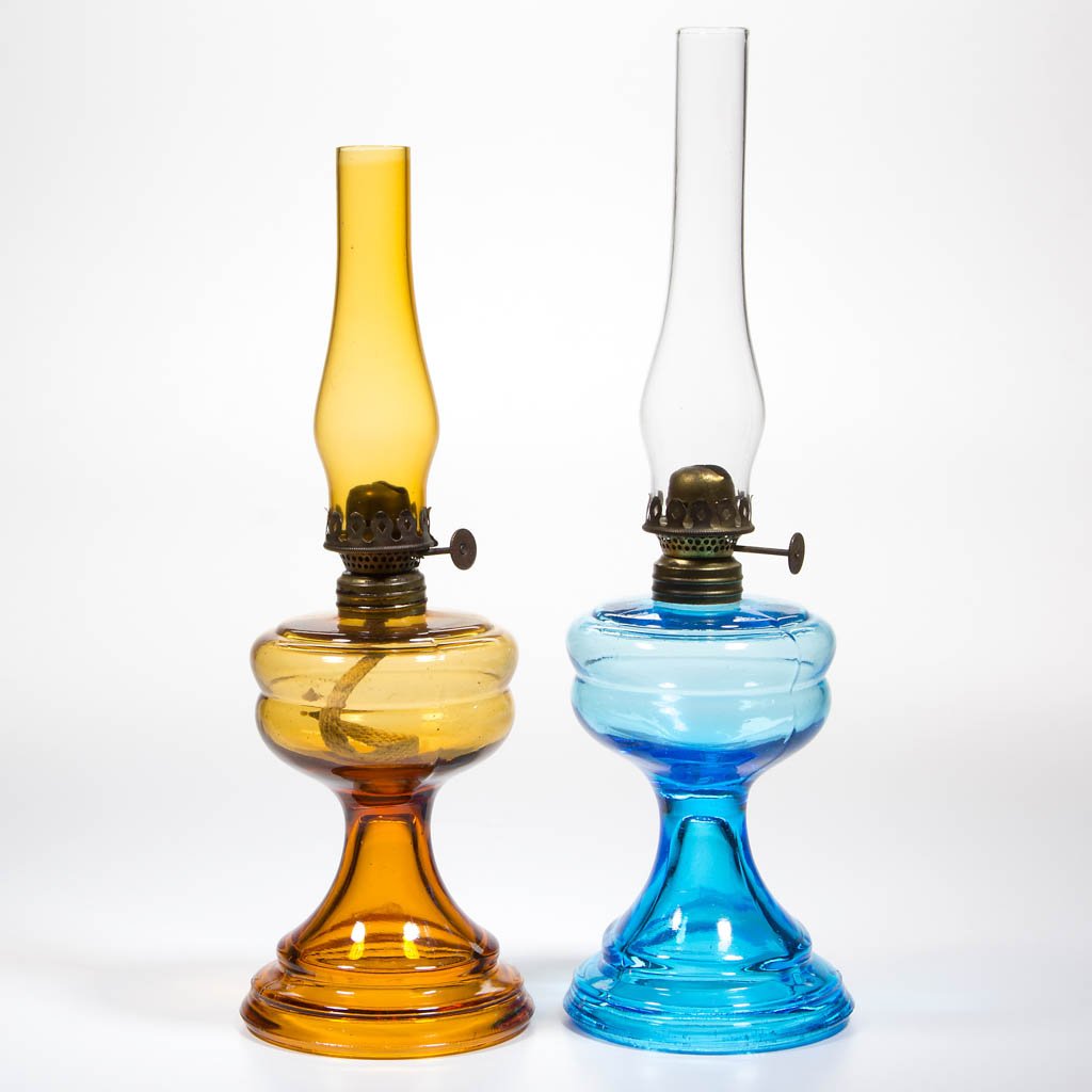 COLORED GLASS MINIATURE STAND LAMPS, LOT OF TWO: COLORED GLASS MINIATURE STAND LAMPS, LOT OF TWO, amber and blue, unpatterned font with ringed shoulder, period collars. Fitted with period Acorn burners, amber and colorless chimneys. Fourth quarter 1