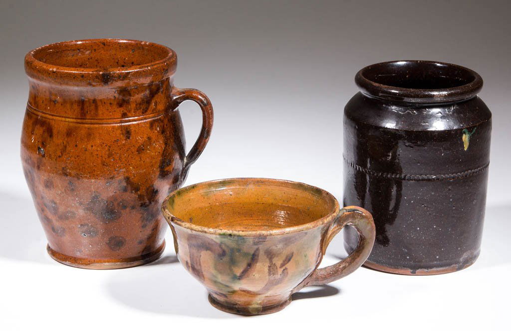 AMERICAN EARTHENWARE / REDWARE DOMESTIC ARTICLES, LOT: AMERICAN EARTHENWARE / REDWARE DOMESTIC ARTICLES, LOT OF THREE, lead-glazed, comprising a porringer with copper and manganese decoration, an ovoid handled jar with manganese decoration, and a cylindri