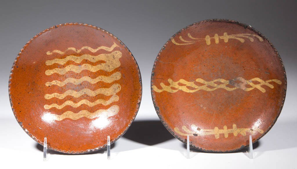 AMERICAN SLIP-DECORATED EARTHENWARE / REDWARE PLATES,: AMERICAN SLIP-DECORATED EARTHENWARE / REDWARE PLATES, LOT OF TWO, lead-glazed, with coggled rims. Yellow-slipped wavy line and stylized clef decorations to centers. First half 19th century. 1 1/4" H,