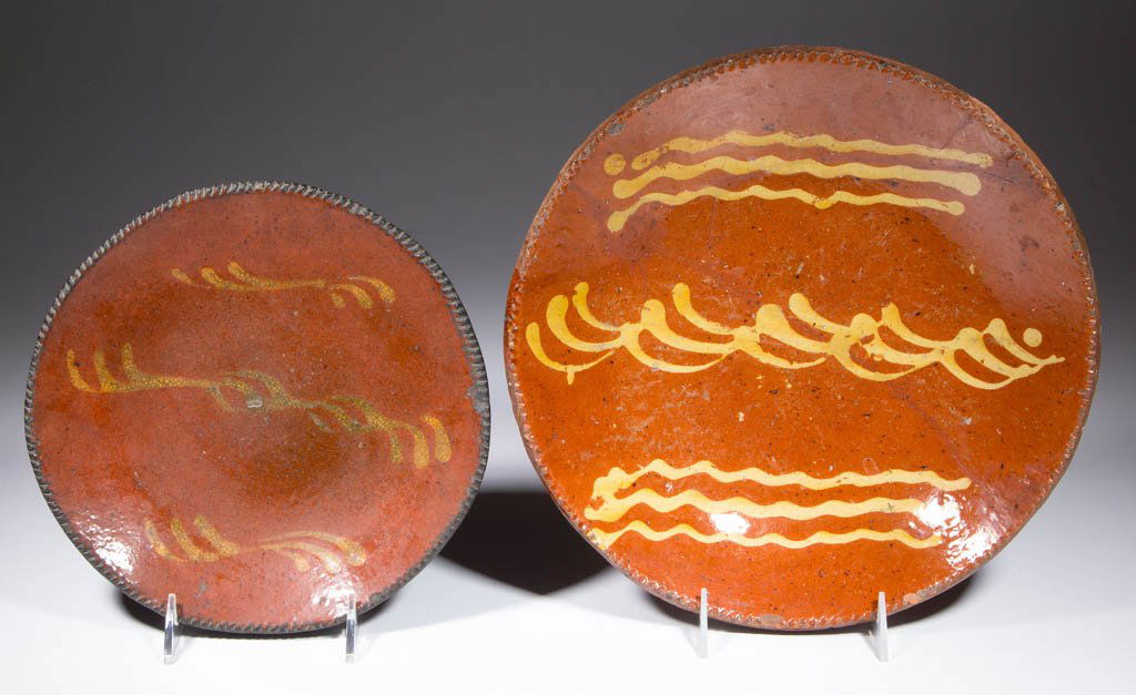 AMERICAN SLIP-DECORATED EARTHENWARE / REDWARE PLATES,: AMERICAN SLIP-DECORATED EARTHENWARE / REDWARE PLATES, LOT OF TWO, lead-glazed, with coggled rims. Yellow-slipped wavy line and stylized clef decorations to centers. First half 19th century. 1 1/2" H,