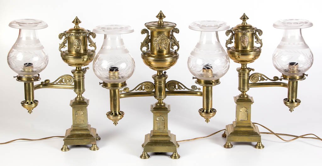 MATCHING SET OF THREE BRASS ARGAND LAMPS: MATCHING SET OF THREE BRASS ARGAND LAMPS, comprising two single-arm and one double-armed example, each with matching complimentary metal overlay decoration and gothic theme, each with a matching cut O