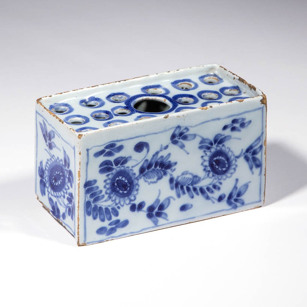 ENGLISH DELFT TIN-GLAZED EARTHENWARE FLOWER BRICK: ENGLISH DELFT TIN-GLAZED EARTHENWARE FLOWER BRICK, having vine and floral designs on sides, blue surrounding the piercing on the top, raised foot on base and raised rim. Unmarked. London / Bristol / L