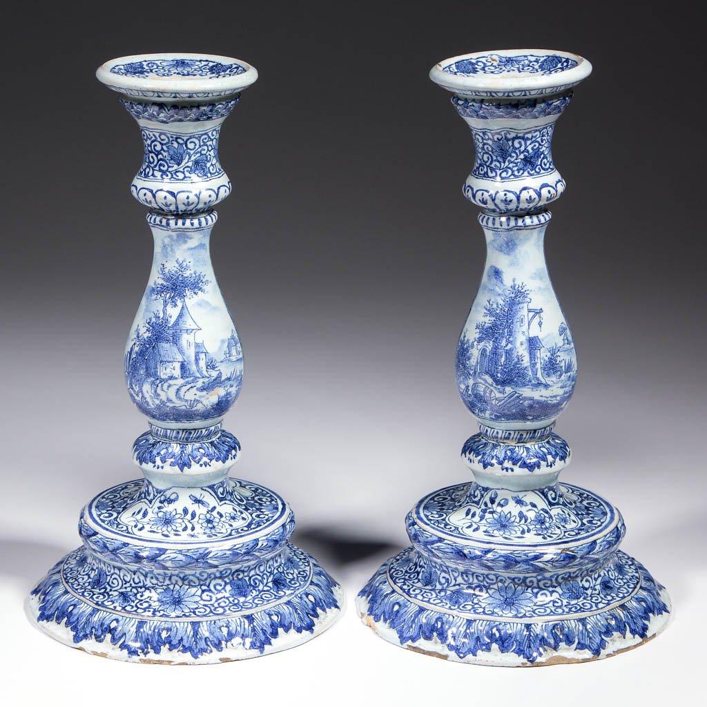 DUTCH DELFT TIN-GLAZED EARTHENWARE CANDLESTICKS, LOT OF: DUTCH DELFT TIN-GLAZED EARTHENWARE CANDLESTICKS, LOT OF TWO, with wide, flaring bases with relief molded acanthus leaves, baluster-shaped central stands, having vignettes of architecture and landscape