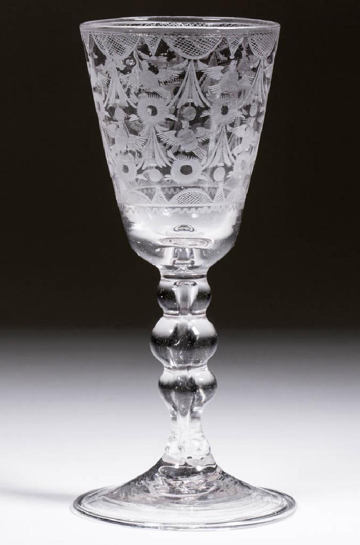 CONTINENTAL FREE-BLOWN AND ENGRAVED BALUSTROID WINE: CONTINENTAL FREE-BLOWN AND ENGRAVED BALUSTROID WINE GLASS, colorless non-lead glass, round pointed funnel bowl heavily engraved with a repeated design of swags, birds in flight, and flower heads, rais