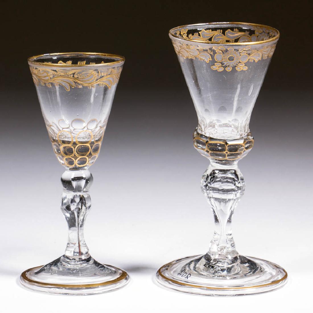 CONTINENTAL FREE-BLOWN, CUT, AND GILDED BALUSTROID WINE: CONTINENTAL FREE-BLOWN, CUT, AND GILDED BALUSTROID WINE GLASSES, LOT OF TWO, colorless non-lead glass, comprising a small example with round pointed funnel bowl, leaves below the rim, cut-facet solid 