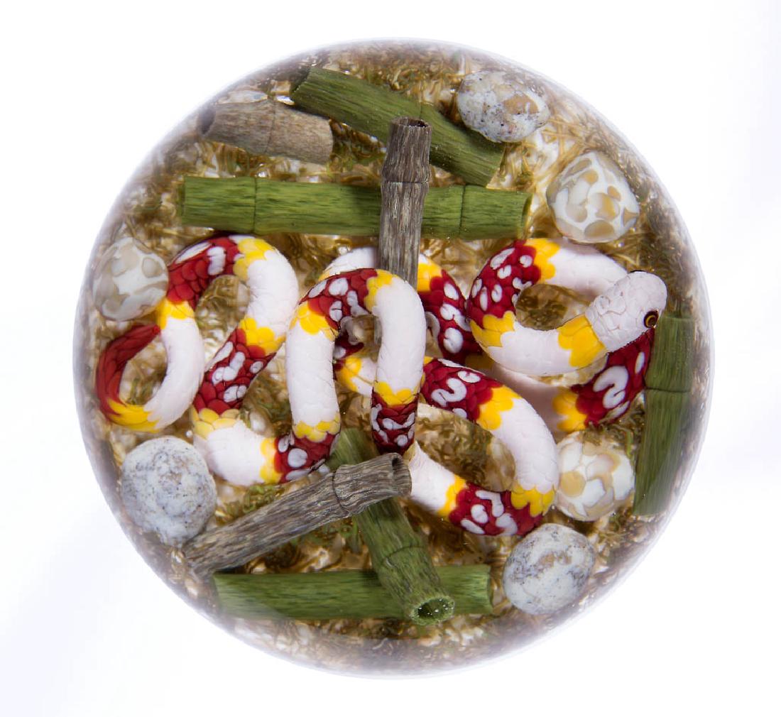GORDON SMITH STUDIO ART GLASS LAMPWORK PAPERWEIGHT: GORDON SMITH STUDIO ART GLASS LAMPWORK PAPERWEIGHT, depicting a long white snake with bands of red and yellow, finely detailed including scales and two-tone eyes, slithering among pebbles and hollow t
